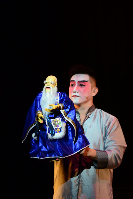Romance of Mistakes an actor with Chinese opera painted face holding a puppet