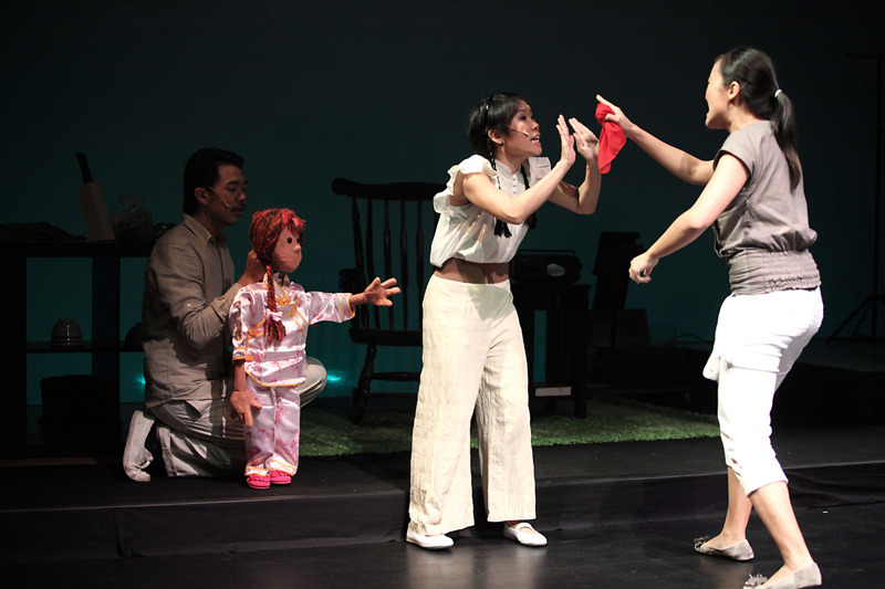 Two actresses fighting with a female child puppet at the back