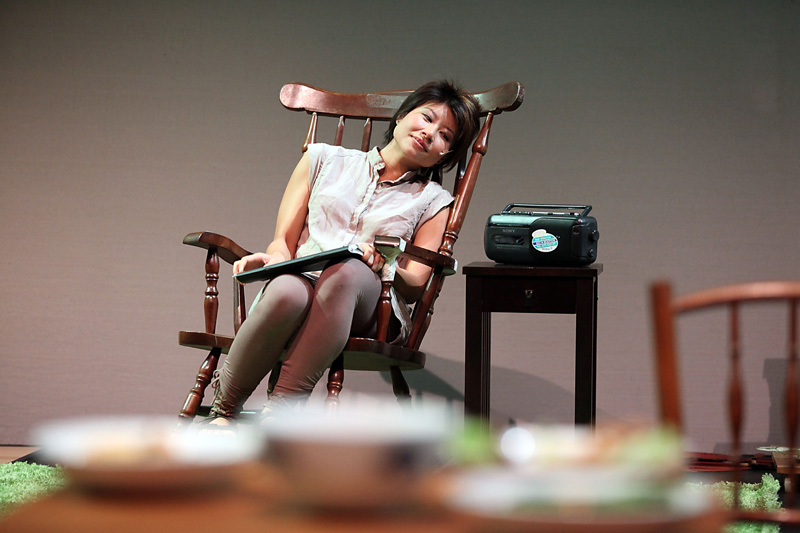 An actress listening to the radio on a rocking chair in Home Boxes