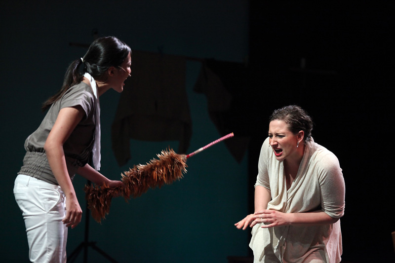 An actress holding feather duster pointing to an actress crouching down