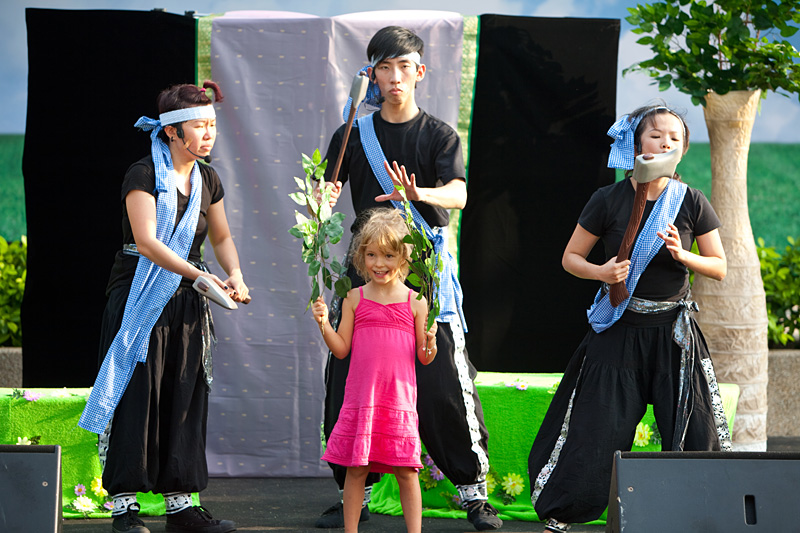 A Caucasian girl holding leaves of the trees interacting with three woodcutter actors in Hug The Tree