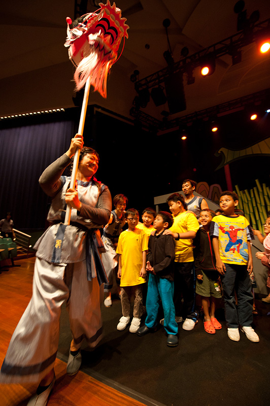 Actress holding head of dragon with children audience in Dragon Dance by Paper Monkey Singapore