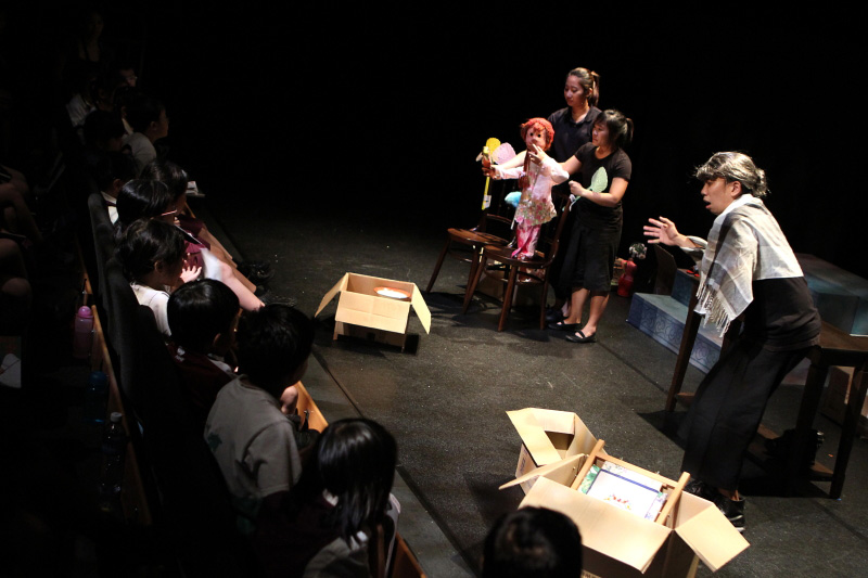 An old lady a girl puppet and boxes in front of audience in The Nonya Nightingale by Paper Monkey Theatre Singapore