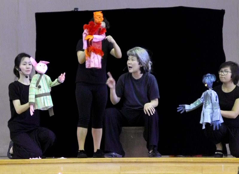 an old lady with three hand puppets in An actress interacting with a hand puppet Feature Image of School Tour Tales by the Moonlight by Paper Monkey