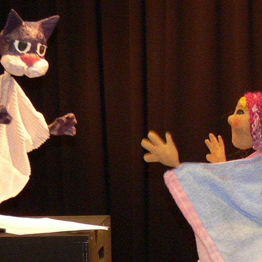 A student holding a cat hand puppet facing a female puppet