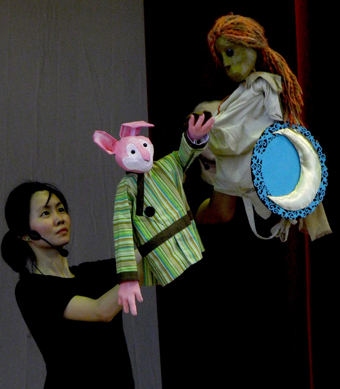 A pink rabbit hand puppet interacting with moon puppet