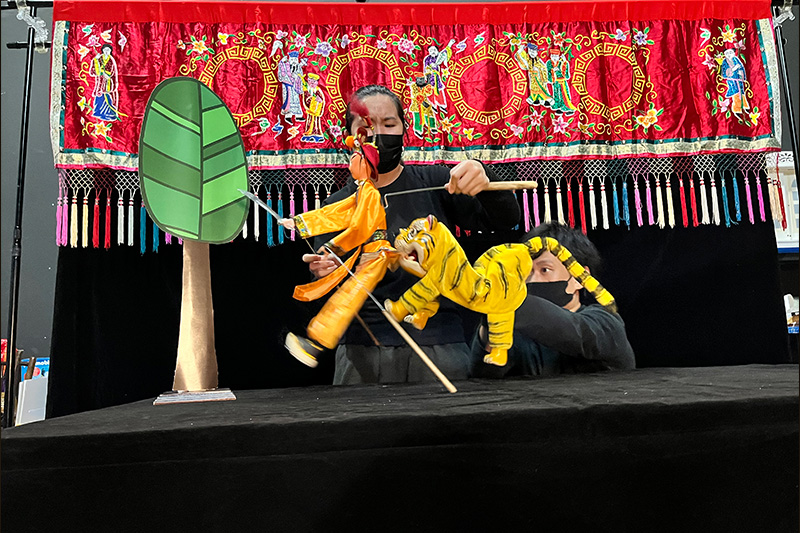 A puppeteer manipulating tiger and Wu Song puppets in School Show The Tiger Hero by PapeA puppeteer manipulating tiger and Wu Song puppets in School Show The Tiger Hero by Paper Monkey Theatre Singaporer Monkey Theatre Singapore