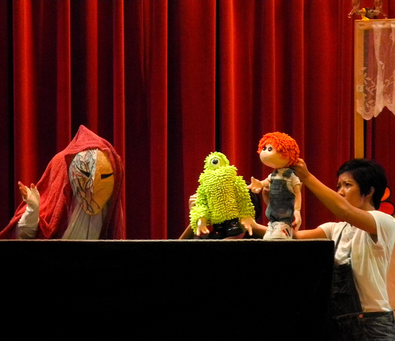 Green puppet monster with Joey talking to a masked character in Monster Under My Bed Community Tour