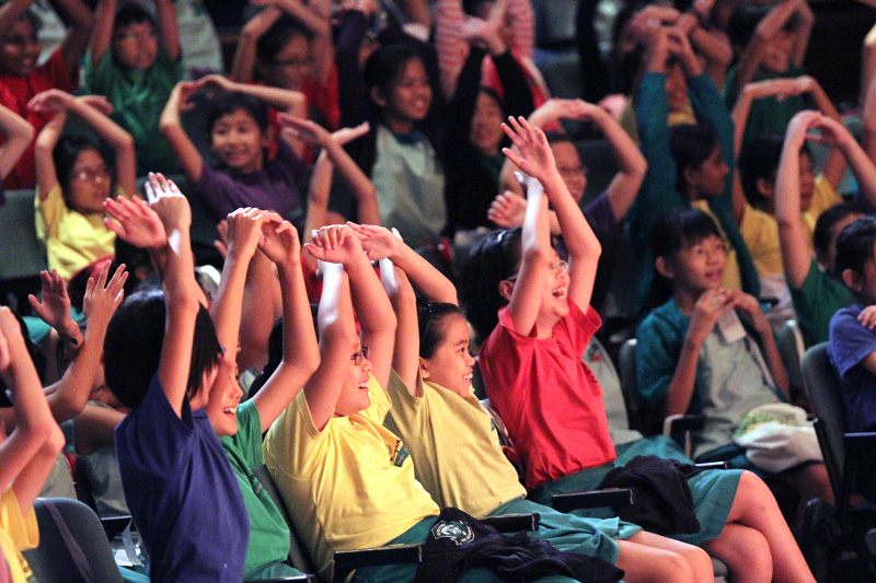 Student audience putting both their hands up above their head happily in Paper Monkey Mercury