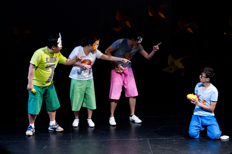 Three actors with masks pointing at a boy kneeling down