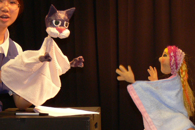 A student holding a cat hand puppet facing a female puppet